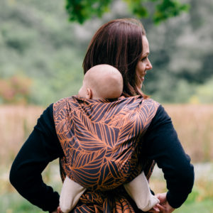 Trageberaterin mit Baby im Tragetuch auf dem Rücken. Bindeweise: einfacher Rucksack. Tragetuch von Fidella